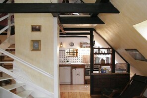 Eine Treppe führt zu einer Küche mit weißen Schränken, einem Spülbecken und einem Holztisch.