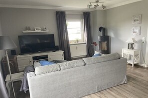 A living room with a sofa, TV, and a wood-burning stove. - Holiday apartment in Zingst with Wi-Fi (Zingst)