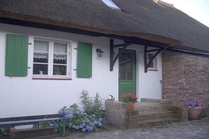 Ein traditionelles, weißes Gebäude mit grünen Fensterläden, einem Strohdach und einer Ziegelwand.