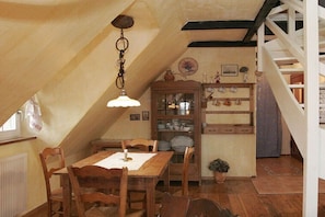 Ein Essbereich mit einem Holztisch, Stühlen, einer Hängeleuchte, einem Schrank mit Geschirr und einer Treppe.