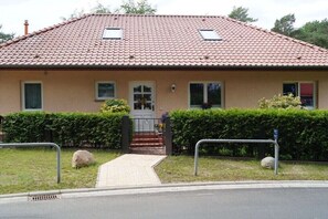 Ein zweistöckiges Haus mit rotem Ziegeldach, einer Haustür und einer kleinen Veranda mit Stufen.