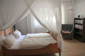 A bed with a canopy, a chair, a bookshelf, and a chandelier in a room with wooden flooring. - Holiday apartment with 1 bedroom (Nordwestuckermark)