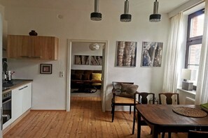 A modern kitchen with wooden cabinets, a dining area with a wooden table and chairs, and a living space with a sofa and artwork on the walls. - Holiday apartment with 1 bedroom (Nordwestuckermark)