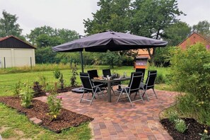 An outdoor patio with a table and chairs, a large umbrella, and a brick pathway. - Holiday apartment with 1 bedroom (Nordwestuckermark)