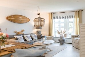 Ein gemütliches Wohnzimmer mit einer Couch, einem Couchtisch, einer Hängelampe und einem Fenster mit Vorhängen.