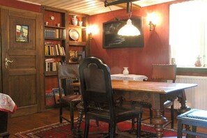 A dining area with a wooden table, chairs, a bookshelf, and a painting on the wall. - The green cottage - Below (Ostseebad Prerow)