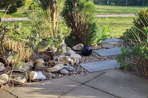 Ein Garten mit verschiedener Pflanzenvielfalt, Steinen und einer schwarzen, kugelförmigen Struktur.