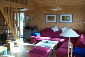 Ein Holzinnenraum mit einer Couch, einem Hocker, einer Lampe und einem Schreibtisch mit einem Computer.