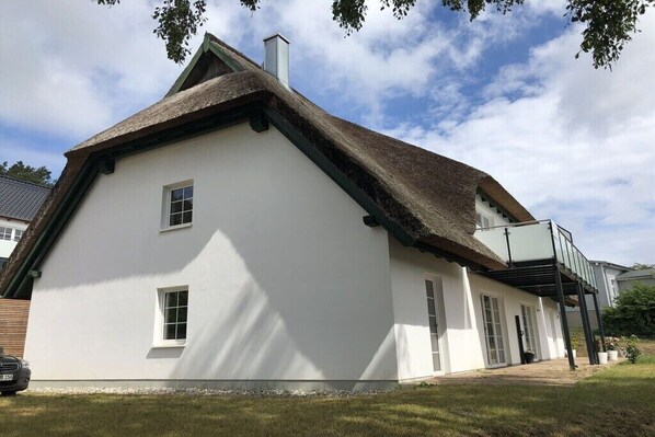 Ein weißes Haus mit Strohdach, einem Balkon und einem kleinen Garten.