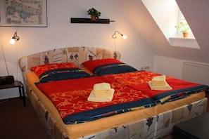 A bed with a red and blue bedspread, two pillows, and a map on the wall. - Dr. Schuldt, Hans-Otto (Waren)