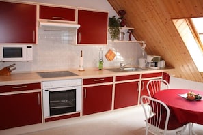 A kitchen with red cabinets, a microwave, an oven, a sink, and a dining area with a red tablecloth. - Dr. Schuldt, Hans-Otto (Waren)