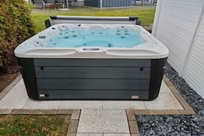 Ein Whirlpool mit schwarzer Außenhülle und weißem Innenraum, auf einer Steinterrasse platziert.