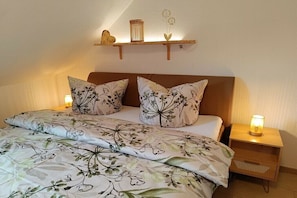 Ein Schlafzimmer mit Bett, floralem Bettbezug, Nachttisch mit Lampe und Regal mit Dekoration.