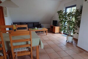 A cozy living room with a sofa, a dining table, a TV stand, and a potted plant. - Holiday apartment with 2 bedrooms (Putbus \/ OT Güstelitz)
