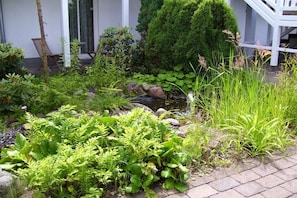 A garden with a pond, various plants, and a small seating area with chairs. - Am Stadtwald, Apt. 8 (Kühlungsborn)