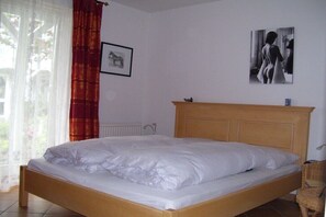 A single bed with a wooden headboard, a framed picture on the wall, and a window with curtains. - Am Stadtwald, Apt. 8 (Kühlungsborn)
