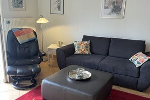 A living room with a sofa, a chair, a lamp, and a tray with a glass. - Am Stadtwald, Apt. 8 (Kühlungsborn)