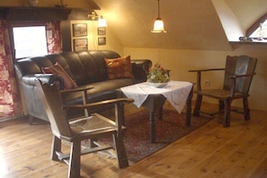 Ein gemütliches Wohnzimmer mit Ledersofa, Holzstühlen, einem kleinen Tisch mit einer Vase und Holzboden.