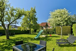Ein Garten mit Rutsche, Schaukel und Glastisch.