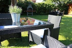 Ein Tisch mit Glasplatte, Korbstühle, ein Blumentopf und ein Grill in einem Hinterhof.