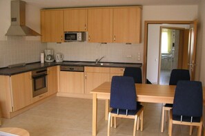 A compact kitchen with wooden cabinets, a microwave, a coffee maker, and a dishwasher. There is a dining table with four chairs. - Holiday apartment with 2 bedrooms (Zingst)