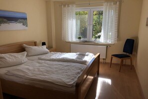 A bedroom with two beds, a window with curtains, a radiator, a chair, and a painting on the wall. - Holiday apartment with 2 bedrooms (Zingst)