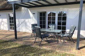 Eine Terrassengaststätte mit Tisch und Stühlen, einem überdachten Bereich und einem weißen Gebäude mit großen Fenstern.