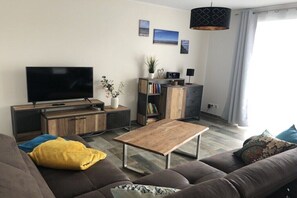 Ein modernes Wohnzimmer mit Flachbildfernseher, Holztisch, Sofa und Bücherregal.