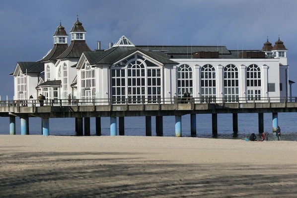 A white pier extending over water with a building featuring arched windows and multiple roof styles. - Holiday apartment in Baabe with swimming pool (Baabe)