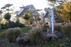 A large, multi-story house with a prominent balcony, surrounded by a well-maintained garden with various plants and flowers. - Holiday apartment in Baabe with swimming pool (Baabe)