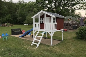 Ein Spielhäuschen aus Holz mit Rutsche, einer Leiter und einer Veranda.