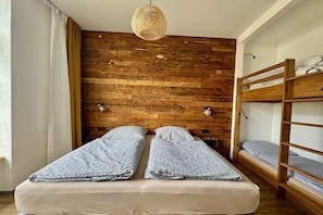 Ein Zimmer mit einer Holzwand, Etagenbetten, einer Hängeleuchte und einem Bett mit gemusterten Bettwaren.