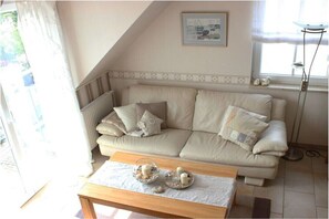 A living room with a beige sofa, a coffee table with decorative items, a framed picture on the wall, and a floor lamp. - Holiday apartment with 2 bedrooms (Graal-Müritz)