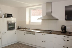 A modern kitchen with white cabinetry, stainless steel appliances, a window, and a built-in range hood. - Holiday home in Grömitz with swimming pool (Grömitz)
