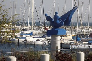 A marina with multiple boats docked, a prominent blue sculpture, and a clear view of the water. - Holiday home in Grömitz with swimming pool (Grömitz)