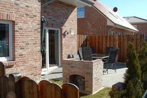 A brick house with a patio, a wooden fence, and a brick fireplace. - Holiday home in Grömitz with swimming pool (Grömitz)