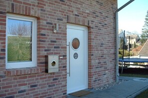A brick building with a white door, a window, and a small outdoor area with a trampoline. - Holiday home in Grömitz with swimming pool (Grömitz)