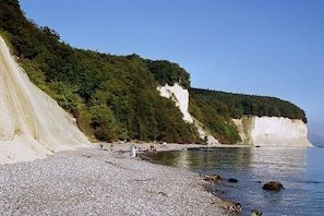 Ein Kiesstrand mit einer weißen Klippe und einem bewaldeten Hang.