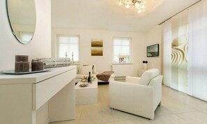 Ein moderner, gut beleuchteter Raum mit einem weißen Sofa, einem kleinen Tisch mit einer Flasche und einem Spiegel an der Wand.