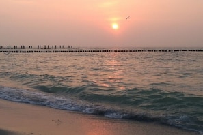 Ein Strand mit Wellen, einem Steg und einem Sonnenuntergang.