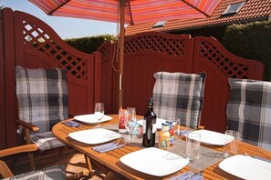 A wooden dining table set for two with plaid chairs, a striped umbrella, and a bottle of wine. - Holiday home in Zingst with swimming pool (Zingst)