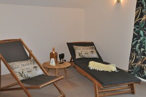 Two lounge chairs with cushions, a small table with a bottle and glasses, and a wall with a plant pattern.