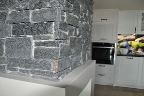 A kitchen with white cabinets, a stone wall, and a countertop with various items.