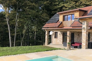 A house with a swimming pool, stone pillars, and a wooden deck.