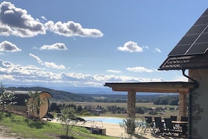 A pool with a pergola, a view of the countryside, and a solar panel on the roof.