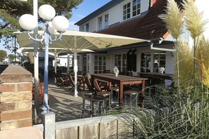 An outdoor seating area with tables and chairs, a lamp post, and a building with large windows in the background. - Apartment in Glowe with swimming pool (Glowe)