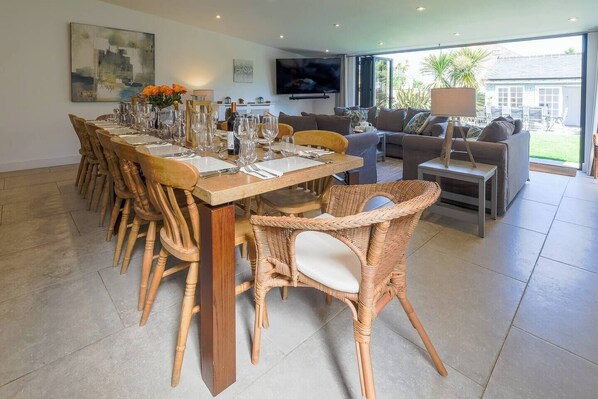 Een eetgedeelte met een lange tafel, gedekt voor een maaltijd, omringd door rieten stoelen.