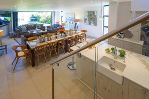 Una cucina moderna con un piano di lavoro in marmo, una zona pranzo con mobili in legno e una scala con ringhiere in vetro.