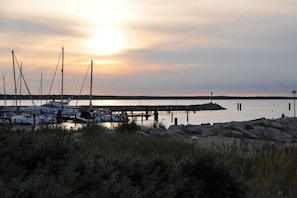 Ein Yachthafen mit vertäuten Booten, eine Pier, die ins ruhige Wasser ragt, und ein Sonnenuntergang im Hintergrund.