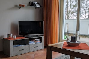 Ein modernes Wohnzimmer mit Flachbildfernseher, Couchtisch und einem Kerzenhalter aus Glas.